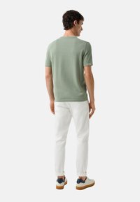 Lichtgroen, kort mouw gebreid shirt, met een textuurafwerking, gecombineerd met witte slim-fit broeken en casual schoenen met een blauwe accent.