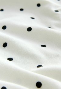 White fabric with small, evenly spaced black polka dots and subtle folds creating soft shadows.