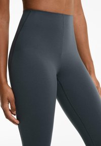 Magas deréku leggings sötétszürke anyagból, sima, rugalmas textúrával és eltérő színű varrásokkal az extra részletesség érdekében.