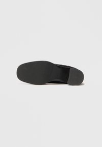 Suola di scarpa nera con superficie in gomma texturizzata; punta arrotondata e tacco leggero. Design minimalista senza loghi o decorazioni visibili.