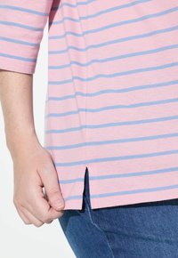 Kortärmad rosa skjorta med blå ränder, med sidoflikar vid fållen. Tillverkad av mjukt material, designen betonar komfort och enkelhet.