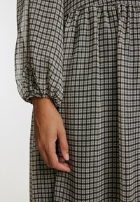 Langärmliges Kleid aus leichtem Stoff mit einem schwarz-weißen karierter Muster, ausgestattet mit elastischen Bündchen und einem gerafften Taillendetail.