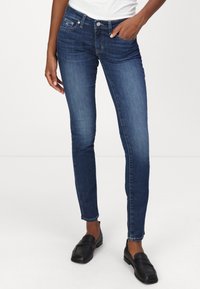 Jeans ajustados azules con una textura suave, diseño clásico de cinco bolsillos, cierre de botón de metal y mínimo desgaste, combinados con mocasines negros.