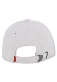 Λευκό καπέλο μπέιζμπολ με υφή, ρυθμιζόμενο λουράκι στο πίσω μέρος και κόκκινη ετικέτα με λογότυπο. Ο σχεδιασμός  είναι απλός και λειτουργικός.