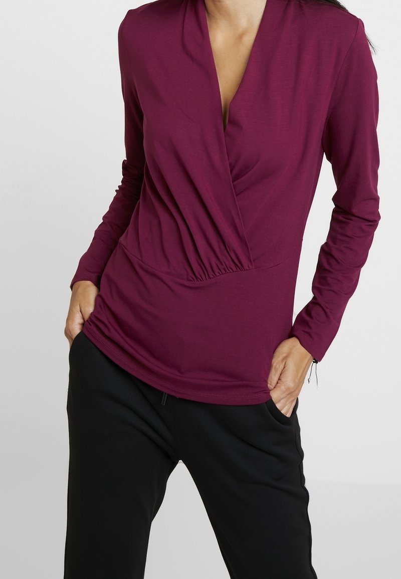 Bordeaux langarmtop met een V-hals ontwerp, met gathers op de taille en een gladde, rekbare stof, gecombineerd met zwarte broek.