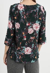 Blommig blus med mörkgrön bakgrund, prydd med stora rosa och blå blommor, trekvartärmar och en avslappnad passform.