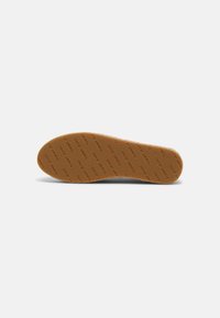 Semelle d'une chaussure beige avec un motif de texte répété "Tommy Jeans" en bas, présentée sur un fond blanc uni.