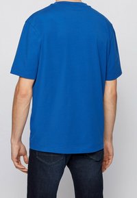 Kortärmad blå T-shirt av bomullsmaterial. Har rund halsringning och avslappnad passform, med minimala sömdetaljer vid fållen.