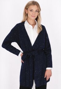 Marinblå stickad cardigan med bälte i midjan, med V-ringning och fläckig struktur. Löst snitt med vida ärmar och sidofickor.