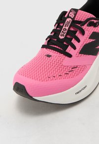 Zapatilla deportiva rosa con parte superior de malla, acentos negros y una entresuela blanca etiquetada como "FRESH FOAM". Presenta un diseño texturizado y cordones.