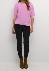 Pull-over rose clair avec manches courtes bouffantes, col et ourlet côtelés, porté avec un jean skinny noir et des bottines marron.