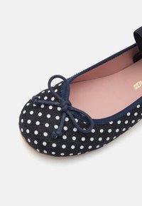 Ballet flat blu e bianco a pois con tomaia in tessuto morbido, punta arrotondata, fiocco decorativo e soletta rosa chiaro.
