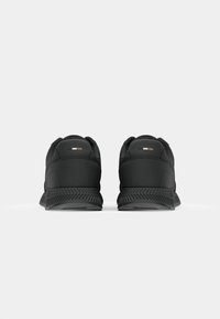 Scarpe sportive nere con una tomaia liscia, collo imbottito e suola in gomma testurizzata. Presentano un piccolo logo vicino al tallone.