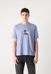 Hele sinine puuvillane T-särk ümmarguse kaelusega ja lühikeste varrukatega, mille keskel on must-valge graafika "Calvin Klein Jeans".
