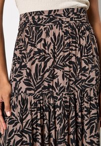 Falda con estampado floral en marrón claro con motivos de hojas negras; presenta una textura fruncida y cintura elástica para mayor comodidad.