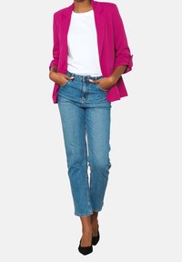 Blazer fucsia sobre una camiseta blanca, combinado con jeans de mezclilla azul claro. Zapatos de tacón alto negros completan el conjunto. Silueta de pierna recta.
