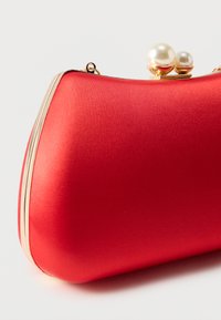 Pochette de soirée en satin rouge avec cadre doré et deux fermoirs décoratifs semblables à des perles sur le dessus, sur fond blanc.
