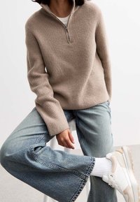 Beige ribbineulaktik, jossa on puoli-vetoketju kaulus, yhdistettynä vaaleansinisiin leveälahkeisiin farkkuihin ja valkoisiin lenkkareihin. Pehmeä tekstuuri ja rento malli.