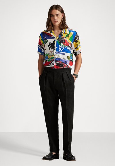 Camisa gráfica de manga corta y multicolor que presenta imágenes y logotipos de carreras, combinada con pantalones negros de cintura alta y zapatos negros.