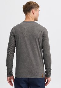 Tricou gri cu mâneci lungi, din material moale, cu decolteu rotund și o etichetă mică din material în partea stângă jos.