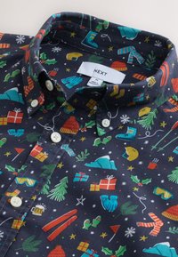 Camicia di cotone con bottoni, sfondo blu scuro, decorata con motivi invernali colorati di regali, alberi e fiocchi di neve.