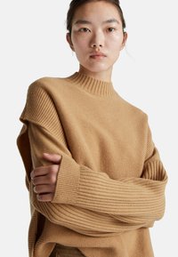 Krémový pletený svetr s vysokým límcem, se žebrovanými rukávy a volným střihem. Hladký povrch s různými vzory pletení.