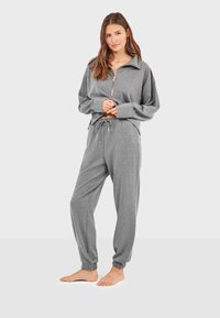 Šedá mikina na zip s límečkem a spadlými rameny, doplněná o sladěné tepláky s elastickým pasem a elastickými lemy u kotníků.
