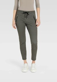 Schwarz-weiße Jogginghosen mit Muster, elastischem Kordelzugbund, seitlichen Taschen und schmalem Schnitt, kombiniert mit weißen Turnschuhen.