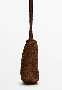 Brązowa pleciona torba o zaokrąglonej podstawie i długim plecionym pasku. Posiada teksturowaną powierzchnię i zebrane otwarcie u góry.