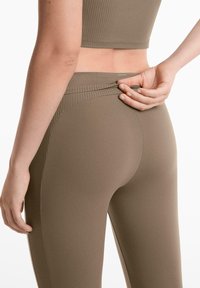Barna, bordázott leggings, amelyeket testhez álló fazon jellemez, sima textúrával és logóval a derékpánt közelében.