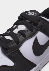 Κοντινό πλάνο μαύρου και άσπρου αθλητικού παπουτσιού Nike με μαύρα κορδόνια, εμφανές το λογότυπο Nike swoosh και το λογότυπο στην γλώσσα του παπουτσιού.