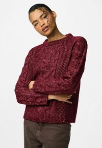 Burgundijas krāsas adīts džemperis ar ribotu tekstūru, ar apaļu kakla izgriezumu un garām piedurknēm. Piemērojumam ir brīvs un īss.