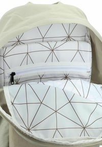 L'intérieur d'un sac à dos beige clair présente un motif géométrique en blanc et marron. Il comprend un compartiment rembourré et une petite poche zippée.