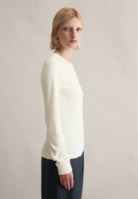Cremefarbenes, geripptes Langarmshirt mit rundem Ausschnitt, figurbetontem Schnitt und weicher Textur, kombiniert mit dunkler Hose. Einfacher und minimalistischer Stil.