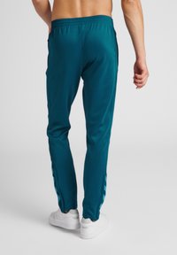 Teal sportieve broek met een tapered fit, voorzien van zijstrepen en een elastische tailleband. Gemaakt van een gladde, lichte stof.