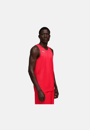 Homme debout portant un haut de sport sans manches rouge Puma et un short rouge assorti sur un fond clair uni.