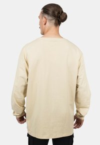 Beige Langarmshirt mit relaxter Passform, Rundhalsausschnitt und strukturiertem Stoff. Die Rückseite hat einen geraden Saum und umgeschlagene Ärmel.