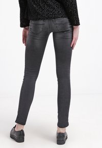 Vaqueros ajustados grises con un acabado desgastado, con tiro bajo y bolsillos traseros, combinados con zapatos de plataforma negros.