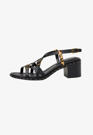 Sort hælsandal med gyldne spænder, leopardmønstret rem, nittet sålkant og blokhæl på hvid baggrund.