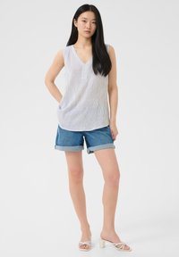 Blusa smanicata leggera a righe con scollo a V; abbinata a shorts di denim arrotolati; la modella indossa sandali bianchi con tacco e cinturini.