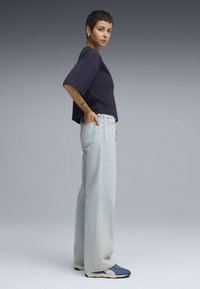 Top cropped azul-marinho com mangas largas, combinado com jeans de perna larga azul-claro. Os sapatos têm uma parte superior azul-escuro com uma sola creme.