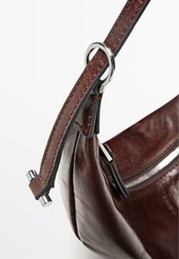 Bruine leren handtas met een gebogen vorm, gevlochten riem met zilveren beslag en een ritssluiting. Soepele textuur en gestikte randen.