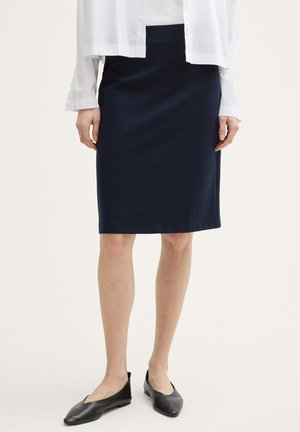 Marineblaue Bleistiftrock aus einem glatten, dehnbaren Stoff. Mit passendem Bund und kurz über dem Knie, kombiniert mit schwarzen flachen Schuhen.