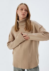 Beżowy sweter z kołnierzem w miękkiej dzianinie, z luźnym krojem, przeskalowanymi rękawami oraz subtelnymi prążkowanymi detalami przy dekolcie.
