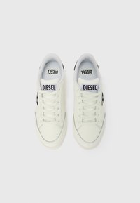 Fehér bőr sportcipők sima textúrával, kerek orral és lapos fűzővel. Oldalukon fekete logóval és kontrasztos varrással díszítve.