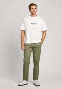 Belega bela bomba majica z belim logotipom "Pepe Jeans London", v kombinaciji z olivno zelenimi hlačami in belimi supergami z črnimi detajli.