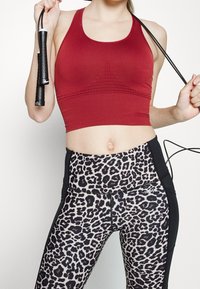 Czerwony, krótki top sportowy z teksturowanym wzorem, połączony z czarnymi legginsami w panterkę oraz czarnym skakanką trzymaną w dłoni.
