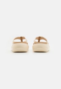 Beige sandals with textured straps and a smooth, light-colored sole. Design features a back strap for support and an open-toe style.