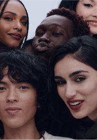 Un gruppo di sei individui con texture e colori di capelli vari, sorridenti su uno sfondo chiaro. Le caratteristiche distintive includono trecce e piercing al naso.