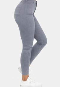 Pantalones ajustados de pana gris combinados con zapatillas blancas, mostrados en modelo de perfil sobre fondo blanco.